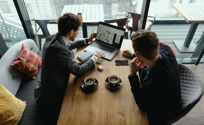 Two business users review an online B2B sales platform on a laptop during a meeting.